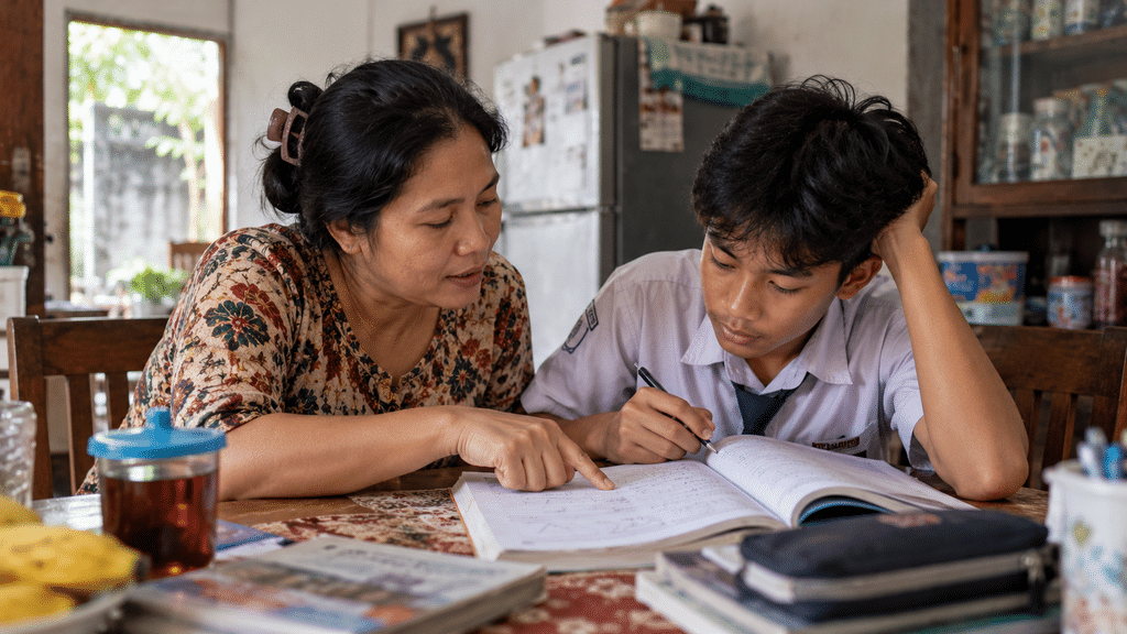 Seorang ibu mendampingi anaknya belajar dan mengevaluasi tugas sekolah bersama di meja ruang tamu rumah.